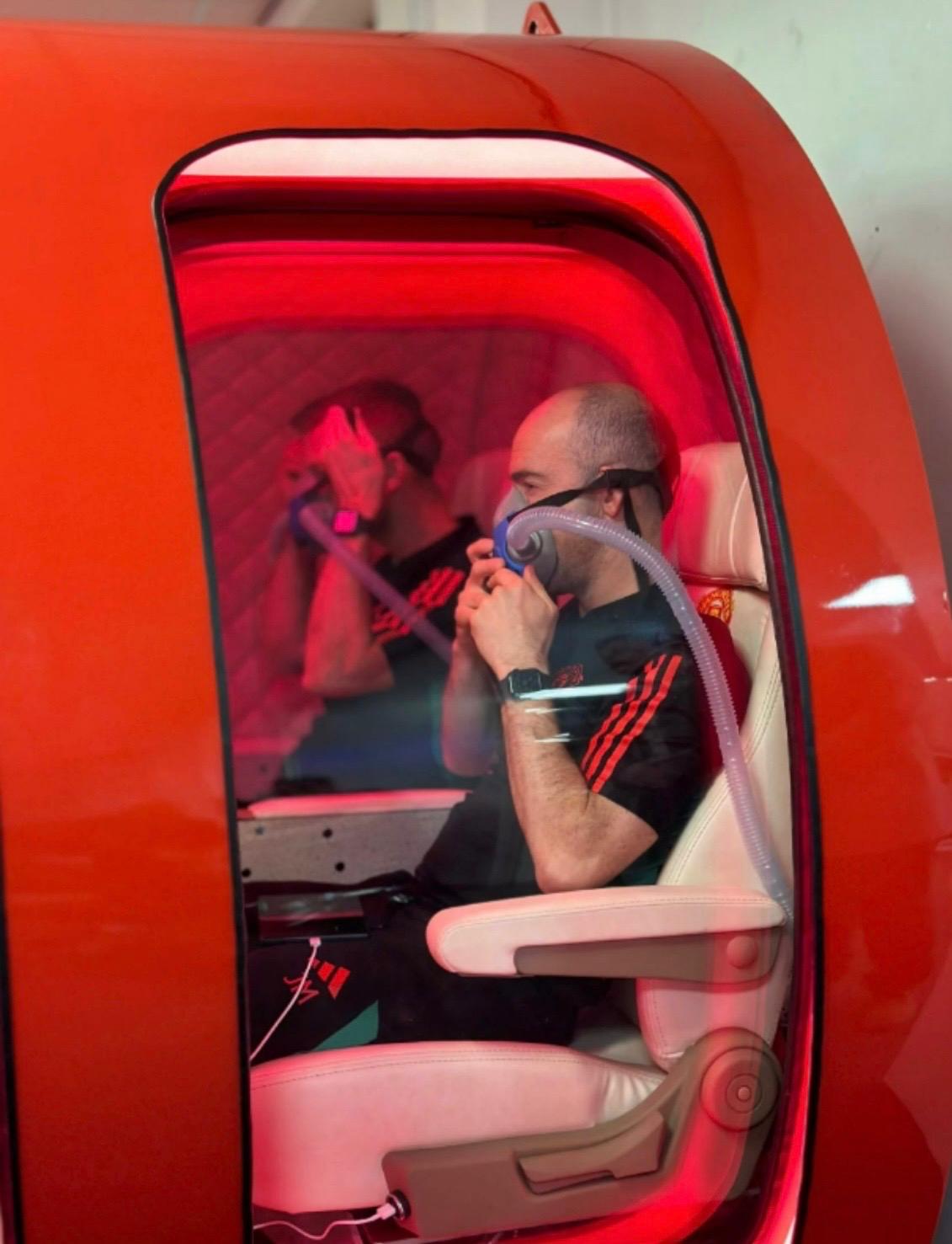 Two athletes inside a Lifemax red-interior chamber wearing oxygen masks during a recovery session.